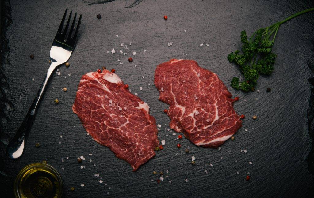 Zwei rohe, marmorierte Stücke vom Ibérico-Schwein auf Schiefer mit Gabel, Salz und Petersilie