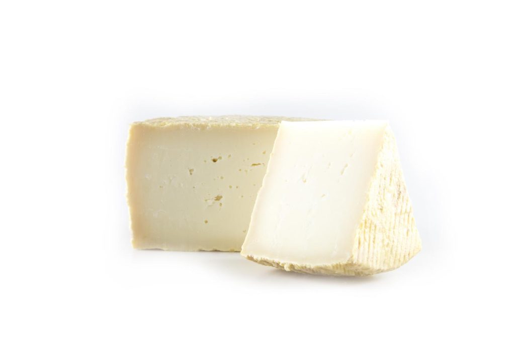 Two wedges of cured goat's cheese with pale ivory paste and natural rind on white