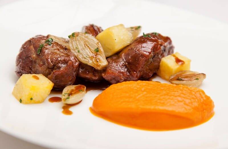 Geschmorte Ibérico-Schweinebäckchen mit Kartoffelwürfeln, Artischocke und orangefarbenem Gemüsepüree