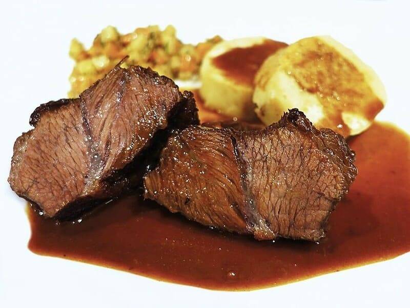 Braised ox cheek pieces in a glossy dark sauce with potato on a white plate