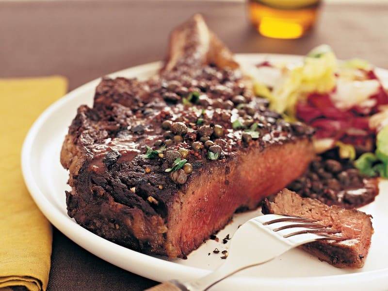 Grilled retinto chuletón crusted with peppercorns on a white plate with salad and a fork