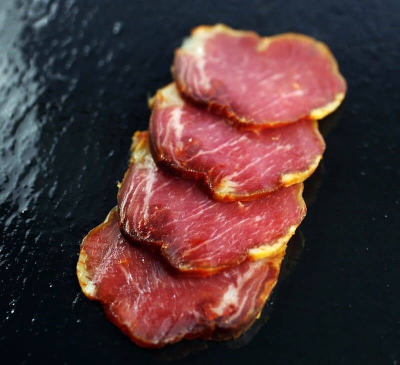 Vier Scheiben luftgetrockneter Lomito Ibérico de Bellota, überlappend auf schwarzem Schiefer