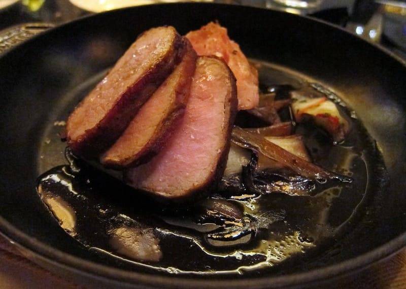 Sliced presa ibérica in a black pan with mushrooms and a dark glossy sauce