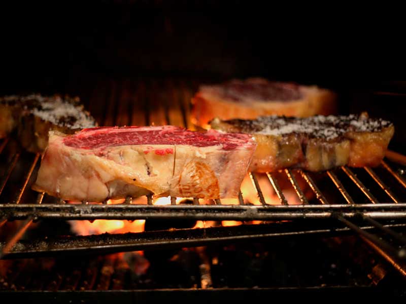 Thick beef steaks sprinkled with coarse salt grilling over open flames on a barbecue grate